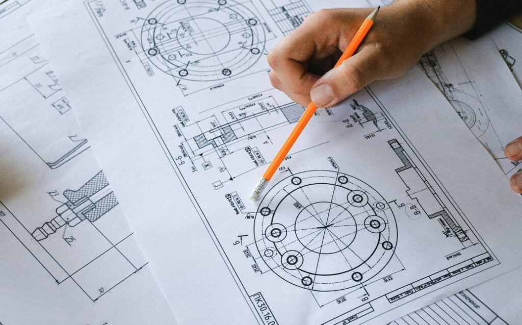 Ruka s tužkou při práci s technickým výkresem.