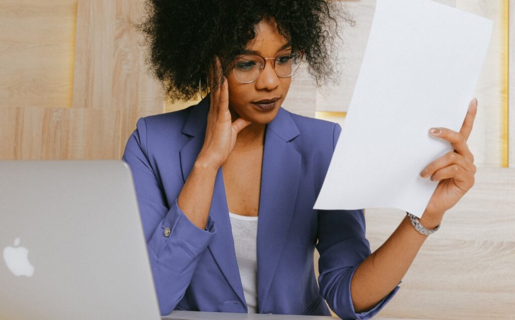 Žena v modrém saku zkoumá dokumenty u notebooku, vyklízení kanceláří a nemovitostí.