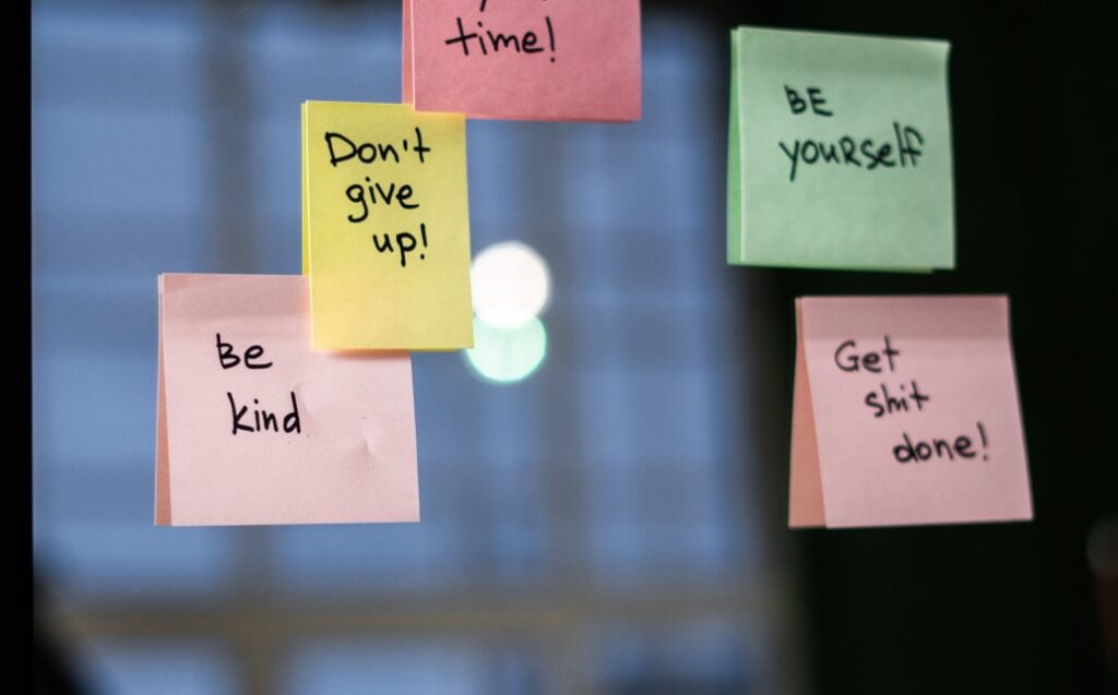 Pozitivní vzkazy na samolepkách: 'Buďte laskaví', 'Nedejte se!', 'Buďte sami sebou', 'Dělejte věci!' připevněné na okně.